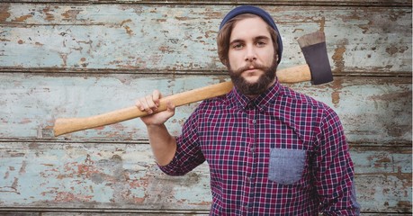 Hipster holding axe while standing against wooden wall