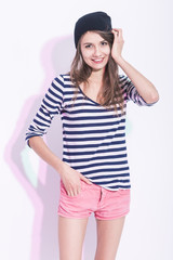 Fototapeta premium Natural Portrait of Happy Laughing Caucasian Brunette Girl in Hat and Striped Shirt. Posing Against White Background.