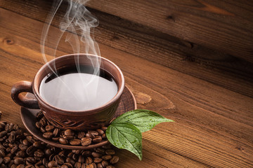 Hot coffee in a clay cup and a plate, whole or ground coffee beans lie on a brown wooden table