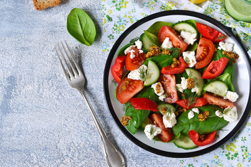 Vitamin salad with tomatoes, spinach and feta cheese on concrete background. Top view.