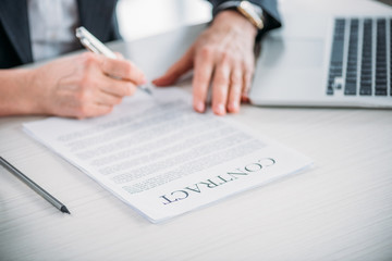 partial view of businesswoman sitting at workplace and signing contract