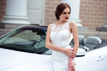 gorgeous bride with fashion makeup and hairstyle in a luxury wedding dress near white cabriolet car