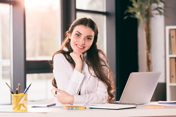 young smiling caucasian businesswoman sitting at table in office and looking at camera