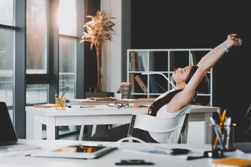 tired asian businesswoman sitting at workplace and stretching arms