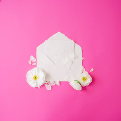 Vintage background. White flowers, petals and paper envelope and card on pink background. Flat lay, top view.