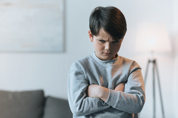 upset little kid boy with arms crossed at home