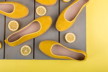 Yellow espadrilles shoes near slices of lemon on wooden background. Top view.