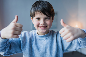 Cute little boy showing thumbs up and smiling at camera