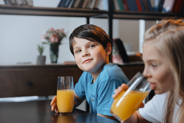 little boy and girl drinking orange juice at kitchen together