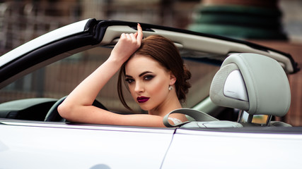 Fototapeta na wymiar gorgeous bride with fashion makeup and hairstyle in a luxury wedding dress in a white cabriolet car