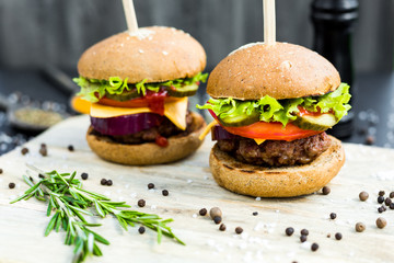 On a wooden board, two beef burgers, black pepper, rosemary, fast food, fashion, on the background of spices in glass bowls, black pepper mill