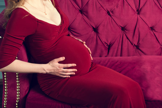Belly of a pregnant woman with hugging hands in a red dress