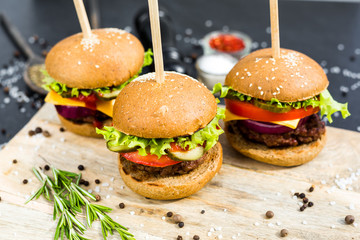 Close-up on a wooden board three beef burgers, with skewers, crispy loaf, lettuce, cheese, tomatoes, cutlets, cucumbers, onions, dark background, delicious, fast food, bright, trendy food, restaurant