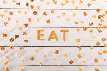 Top view of word eat from breakfast cereal letters and alphabet corn flakes on wooden table