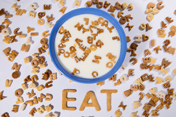 Top view of breakfast cereal alphabet, milk in bowl and word eat isolated on grey