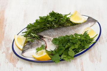 raw fish with herbs and lemon on dish on wooden background