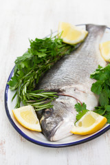 raw fish with herbs and lemon on dish on wooden background