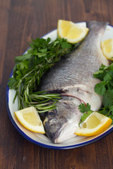 raw fish with herbs and lemon on dish on wooden background