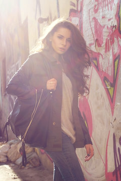stylish elegant girl wearing jacket and jamper with black leather bag posing against urban city wall