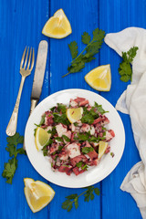 octopus salad with lemon on white dish on wooden background