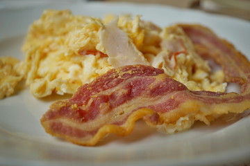 Macro detail of a typical English and American breakfast made of crispy bacon strips and scrambled eggs 