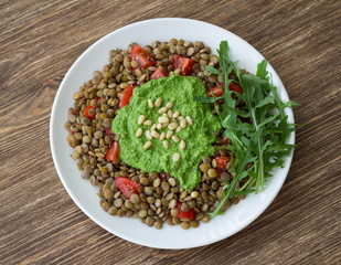 Homemade lentils with tomatoes and pesto sauce from arugula on a wooden background. Delicious healthy food