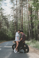 Fototapeta na wymiar Young Caucasian couple on a motorcycle on the forest road. Love, freedom, togetherness concept. Couple travel on a motorbike