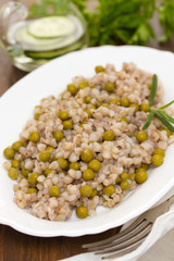 buckwheat with peas on white dish on wooden background
