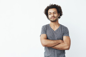 Portrait of stong and handsome african man looking left posing with crossed arms over white wall. Confident startup concept.