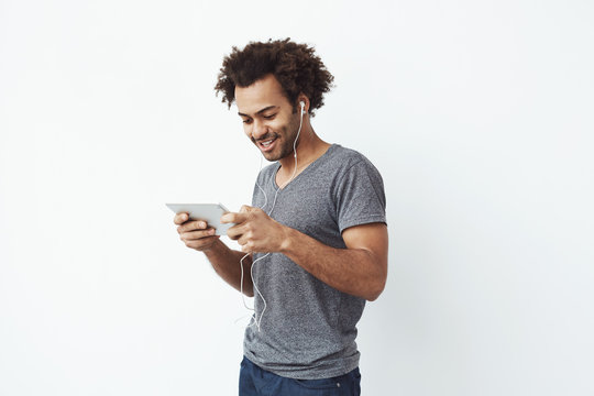 Funny african man in headphones smiling laughing looking at tablet over white background.