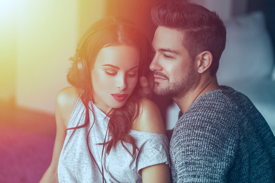Young couple listening music by headphones together at home in sunset