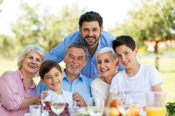 Family sitting at table outdoors, smiling
