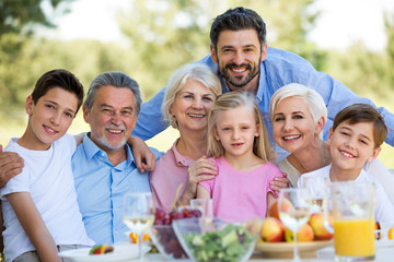 Family sitting at table outdoors, smiling
