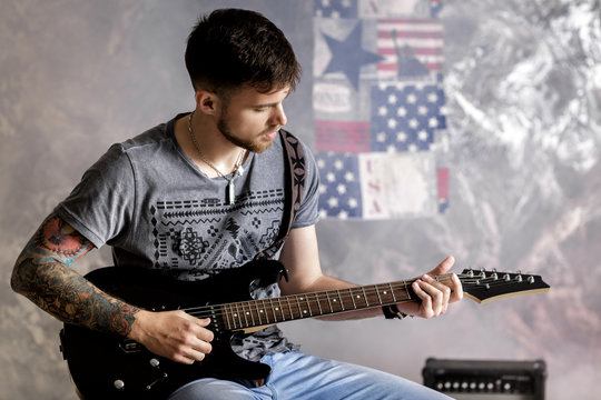 Young handsome musician playing electric guitar on dark background