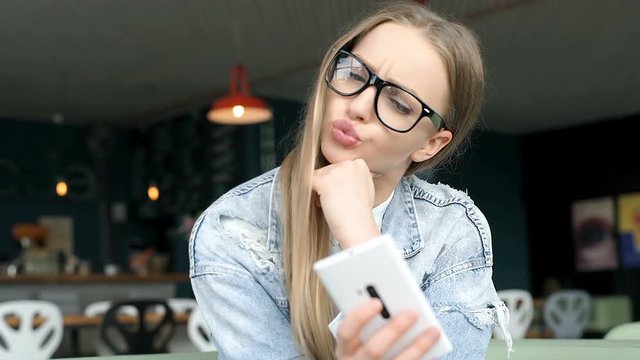 Beautiful girl sitting in the bistro and doing selfies on smartphone, steadycam shot
