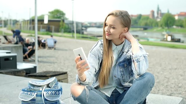 Beautiful girl sitting with her legs crossed and doing selfies on smartphone
