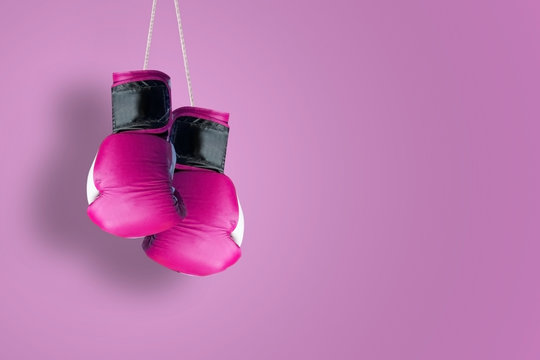Pink hanging boxing gloves hanging against a pink background. Empty copy space for Editor's text.