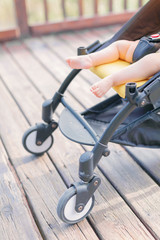 Close-up of stroller with newborn baby sleeping outdoors on wooden pathway in park