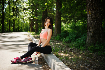 Fitness sport girl in sportswear sitting at road in park with water at bottle, outdoor sports, urban style.