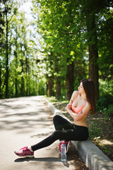 Fitness sport girl in sportswear sitting at road in park with water at bottle, outdoor sports, urban style.