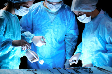 Medical team performing operation. Group of surgeon at work in operating theatre toned in blue