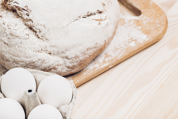 Fresh baked bread, flour and eggs on wooden table. soft light