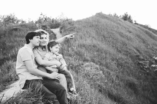 Happy Family Of Three Sitting On The Hill In Summer Time - Black And White. Love, Vacations And Happy Family Concept.