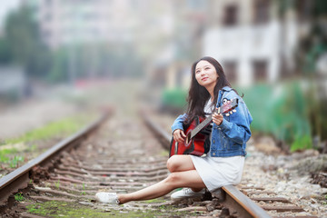 Girl playing guitar on railway tracks.
