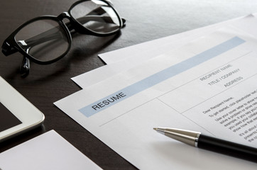 Close-up resume, pen, digital tablet, eyeglasses and business card on wooden desk.