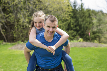 portrait of a father carrying teen girl on back at the park