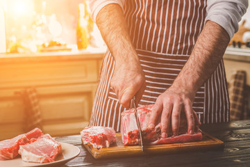 Man cuts of fresh piece of beef on a wooden cutting board in the home kitchen