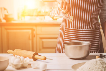 Young woman pouring oil into a bowl with dough, close-up