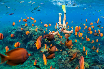 Happy family - girl in snorkeling mask dive underwater with tropical fishes in coral reef sea pool....