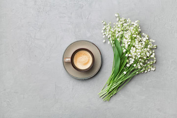 Coffee mug with bouquet of flowers lily of the valley on gray stone table from above in flat lay...